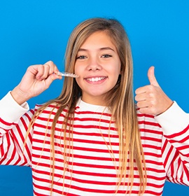 Teenager in red and white striped sweater giving thumbs up holding Invisalign