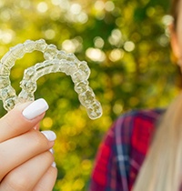 Young woman with white painted nails outside holding Invisalign
