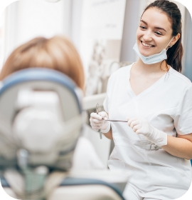 Female dentist in mask smiling at patient in dental chair